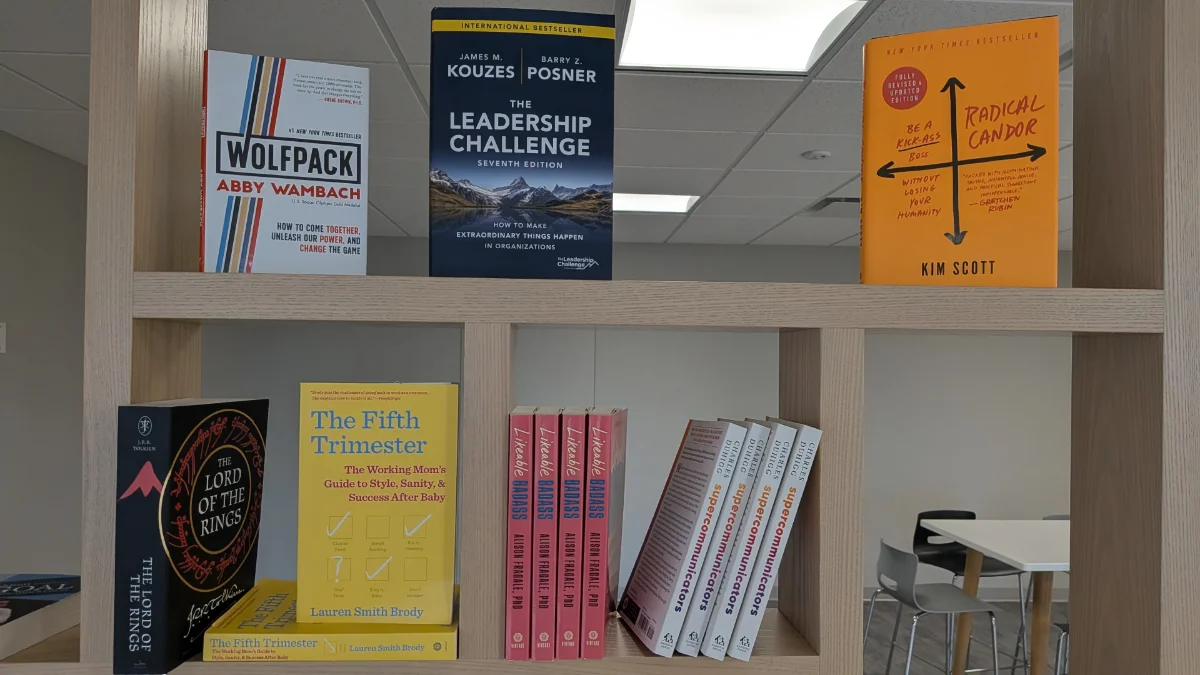 A shelf of books including The Fifth Trimester and Supercommunicators at a team book swap